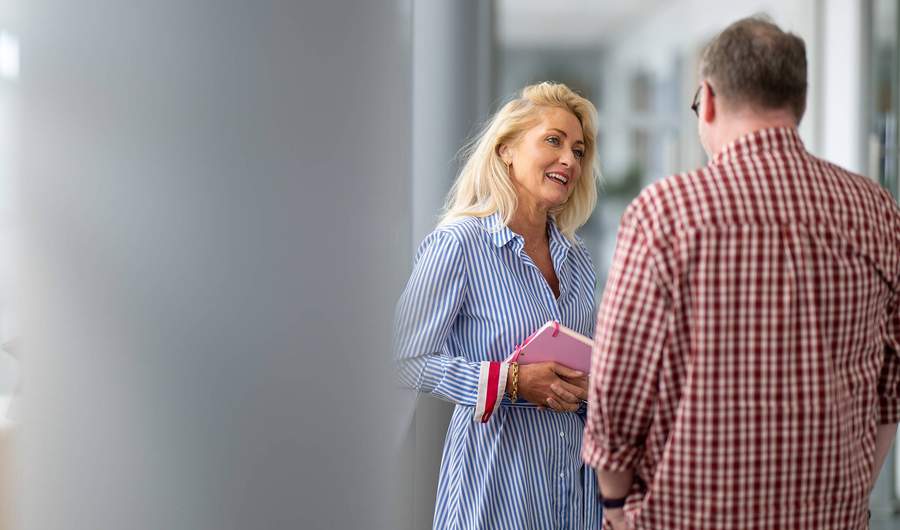 A woman and a man engaged in conversation. The woman is holding a notebook in her hands.