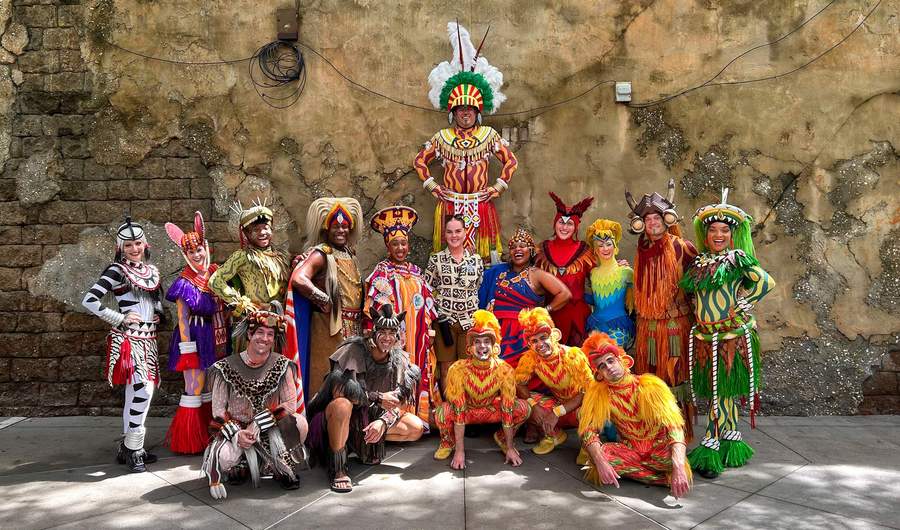 A diverse group of people in vibrant costumes, smiling and posing together for a group photo.