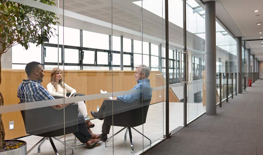 Three people sit facing one another in chairs during a meeting.