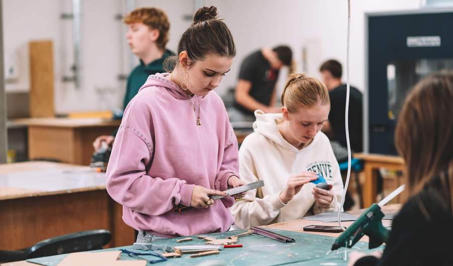 Students working at a table cutting materials and assembling small card models in a workshop.