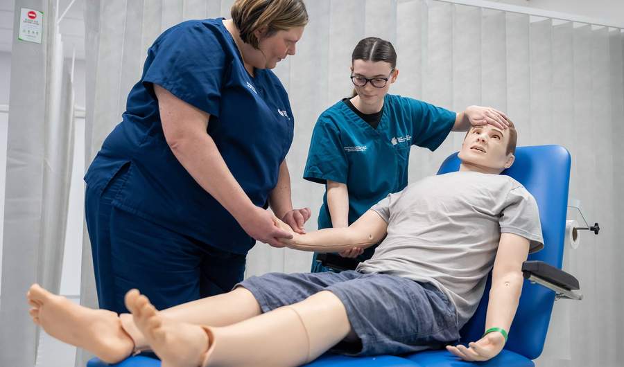 A lecturer demonstrates how to measure a patient's pulse using a manikin.