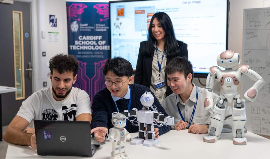 A group of people sit at a table. In front of them is a selection of small humanoid robots.