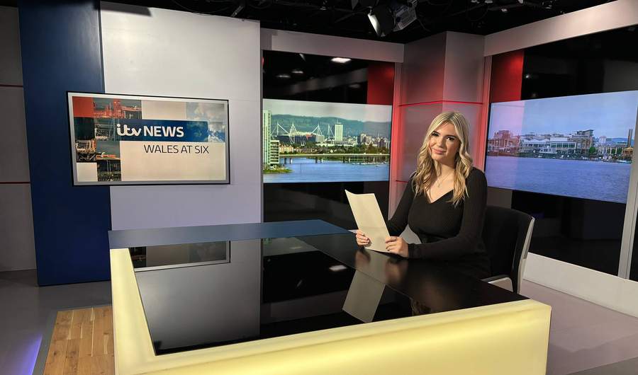 A person sat at a desk in a television news studio.