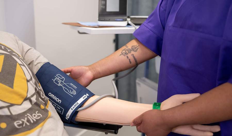 Nursing student places blood pressure cuff on manikin