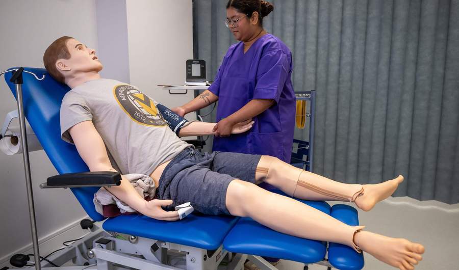 Nursing student places blood pressure cuff on manikin