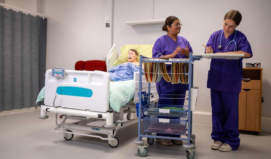 Nursing students with cart next to manikin in bed