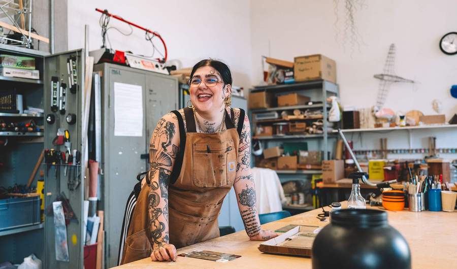 A student leans on a workbench. Behind them are metal cabinets, shelves and a variety of tools, including screwdrivers and spirit levels.