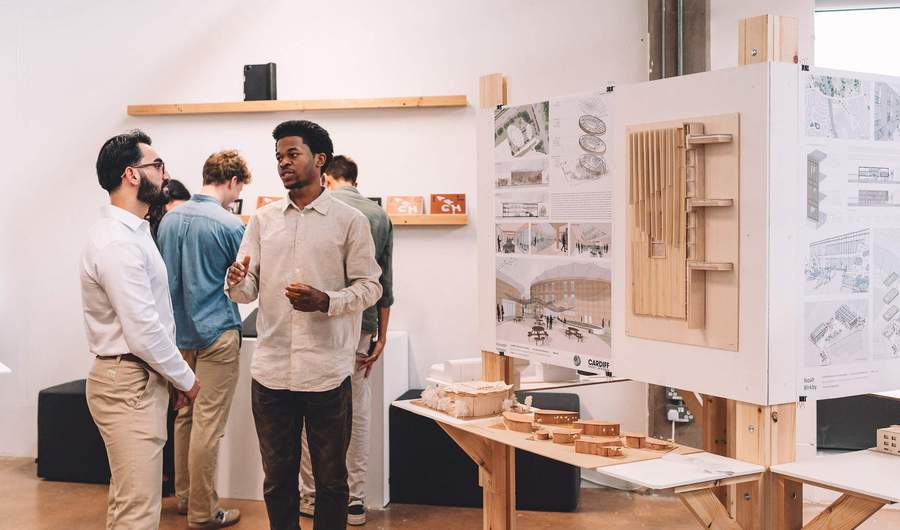 Two people stand beside a table featuring a display of architectural models, engaged in conversation.