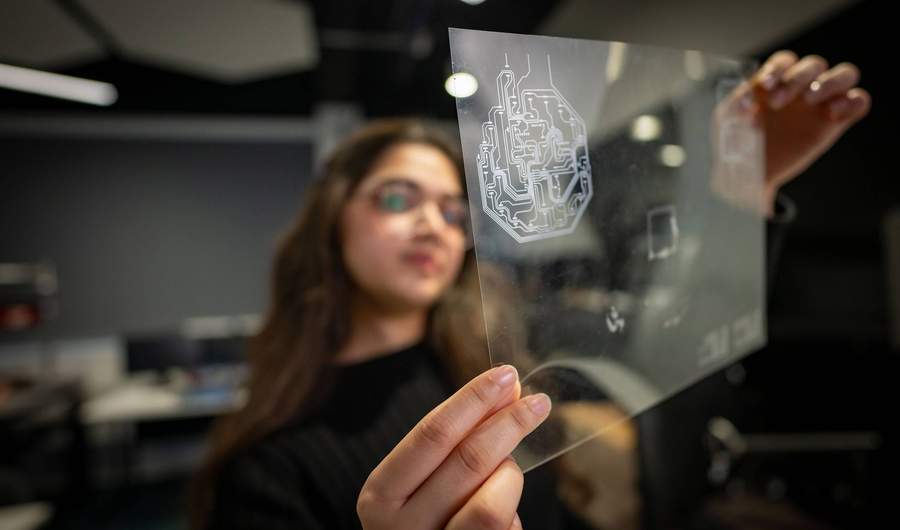 A person holds a small transparent sheet, etched with electronic circuits.