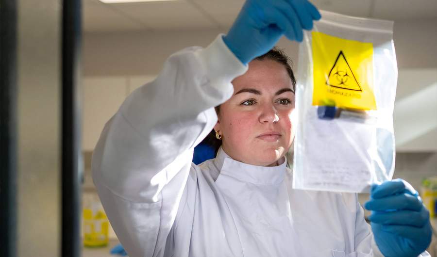 Student in laboratory coat holds clear bag containing test tube