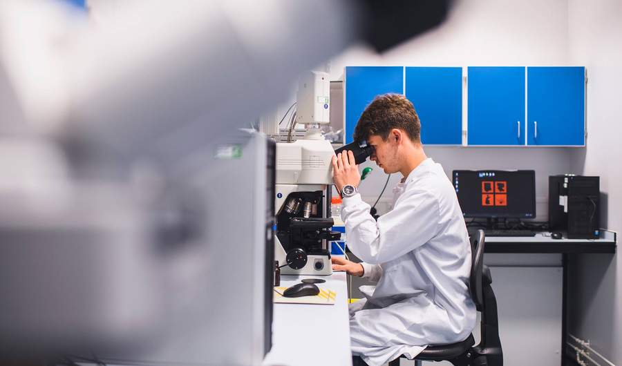 Student in laboratory coat looking through microscope