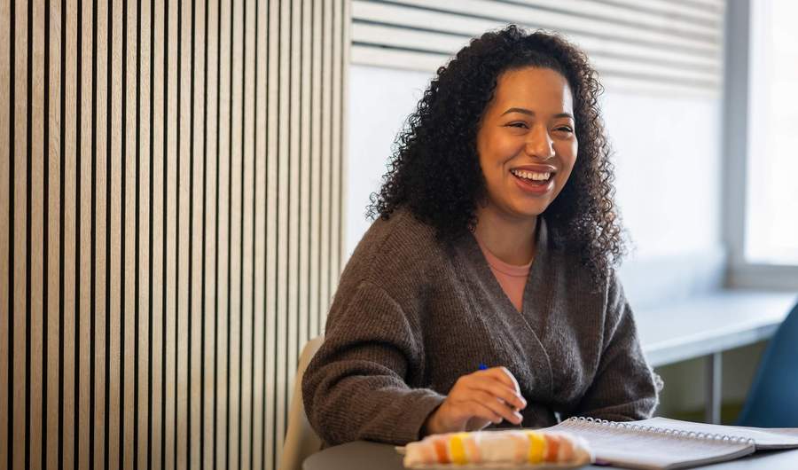 A young woman sits and smiles at a table while working with a pen and pad of paper.