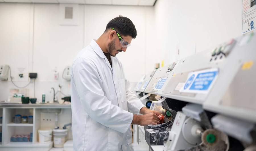 A young adult in white laboratory uniform uses a machine to shape a dental prosthetic.