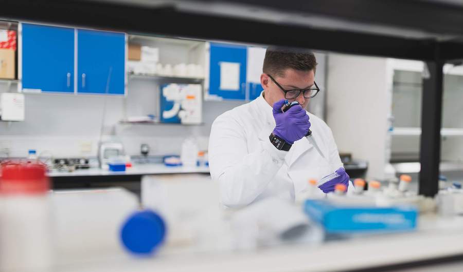A person in a lab coat uses a pipette to dispense a sample into a container.