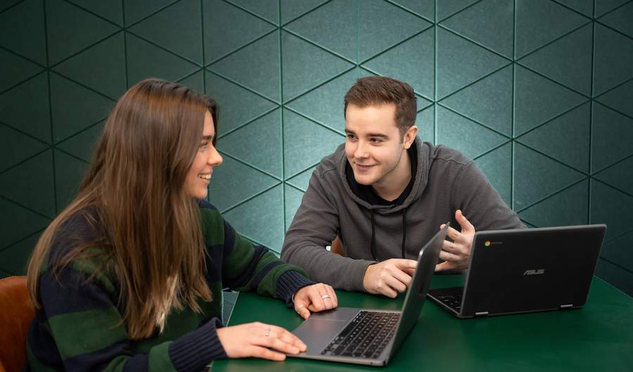 Two students with laptops in conversation