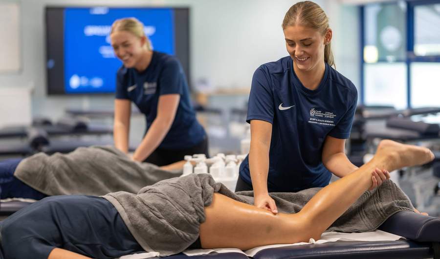 Two sports therapy students practice massage techniques on a patient in a training environment.