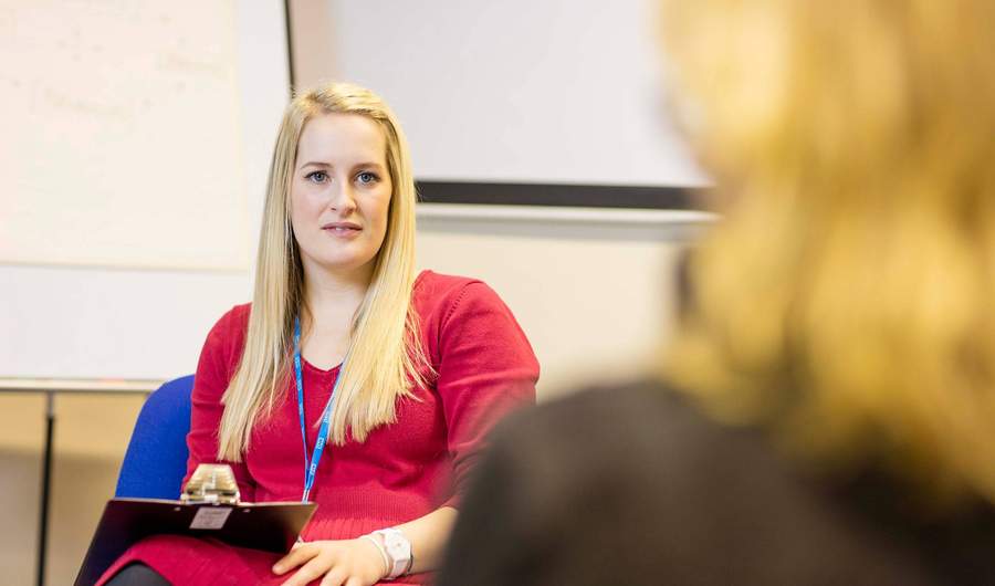 A woman wearing a lanyard with the NHS logo holding a clipboard.