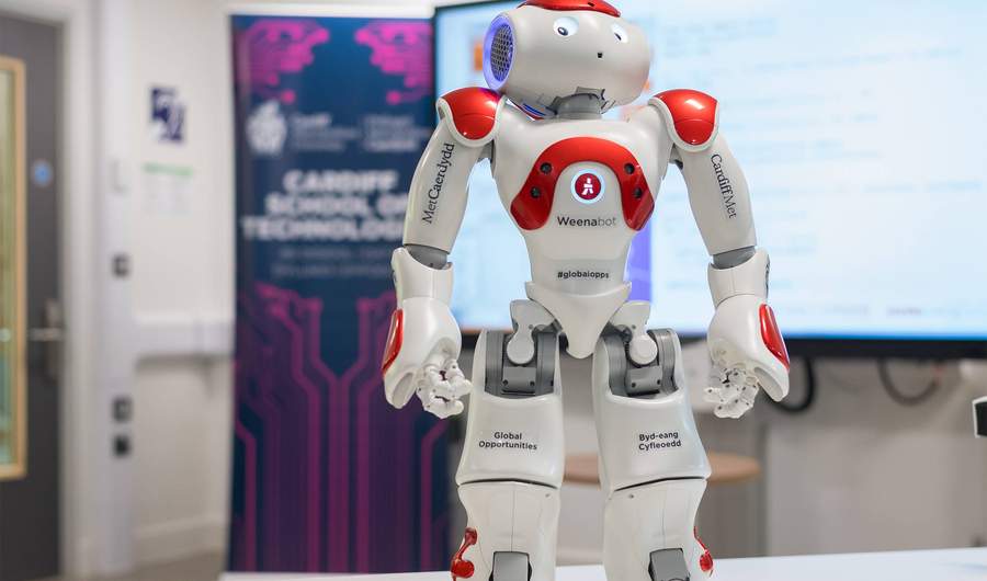 A close-up of a small humanoid robot. The robot has the Cardiff Met logo printed on its arms.