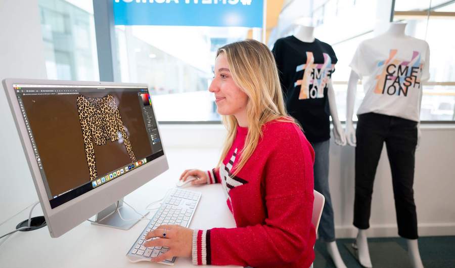 A person sat at a desk in front of a Mac computer.