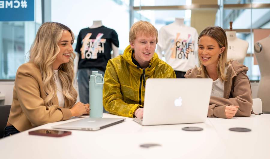 Three people sit alongside each other at a table with laptop computers.