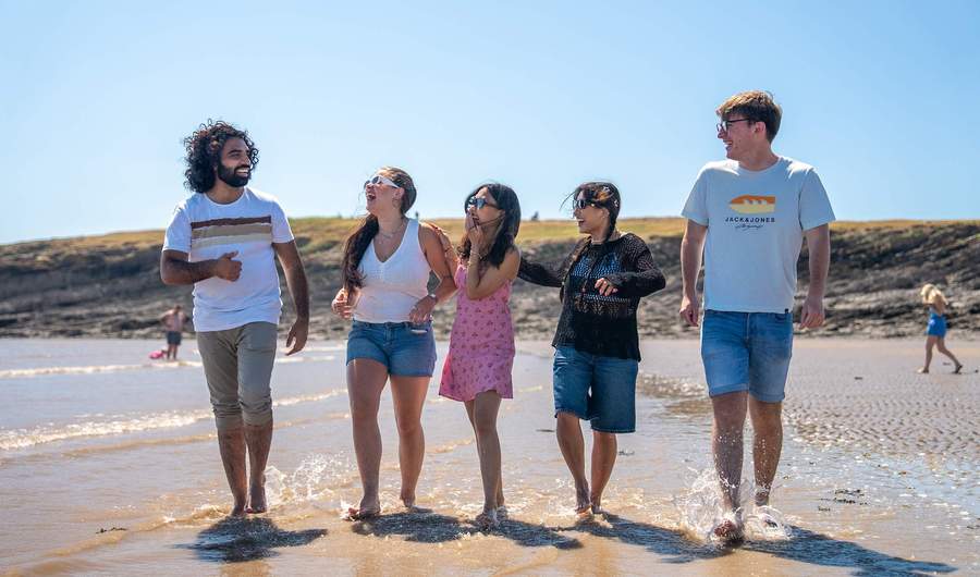 A group of people walking along the sandy beach, enjoying the sun and ocean waves in the background.