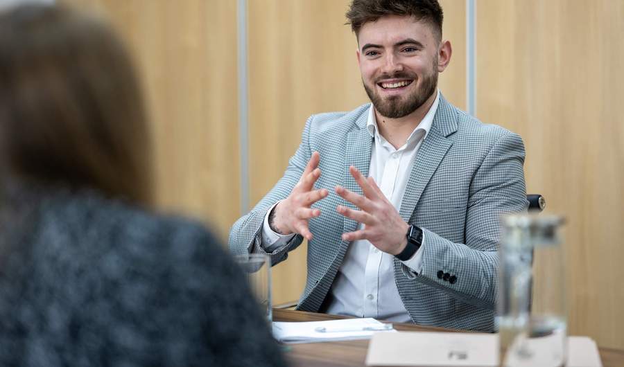 A person in a suit speaks to another person, both appearing engaged in a discussion.
