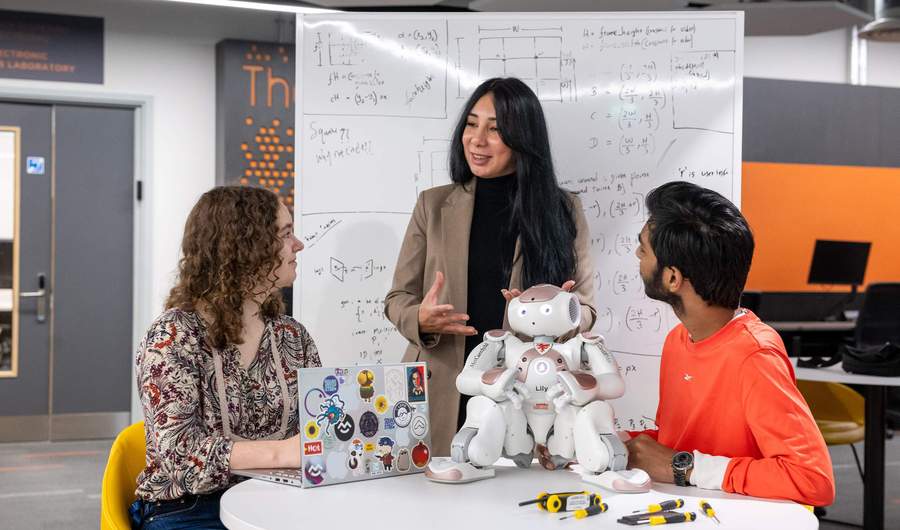 Three people are gathered in discussion. On the table in front of them is a small humanoid robot.