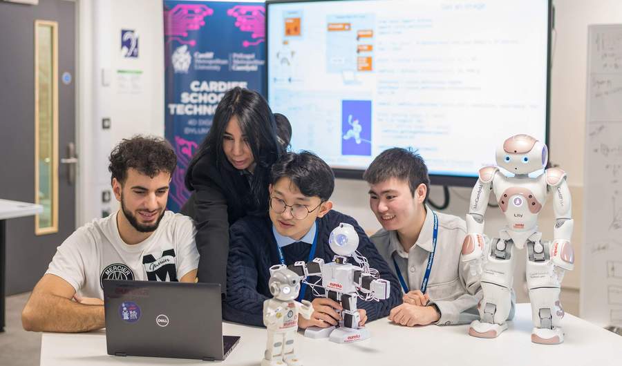 A group of people sit at a table. In front of them is a selection of small humanoid robots.