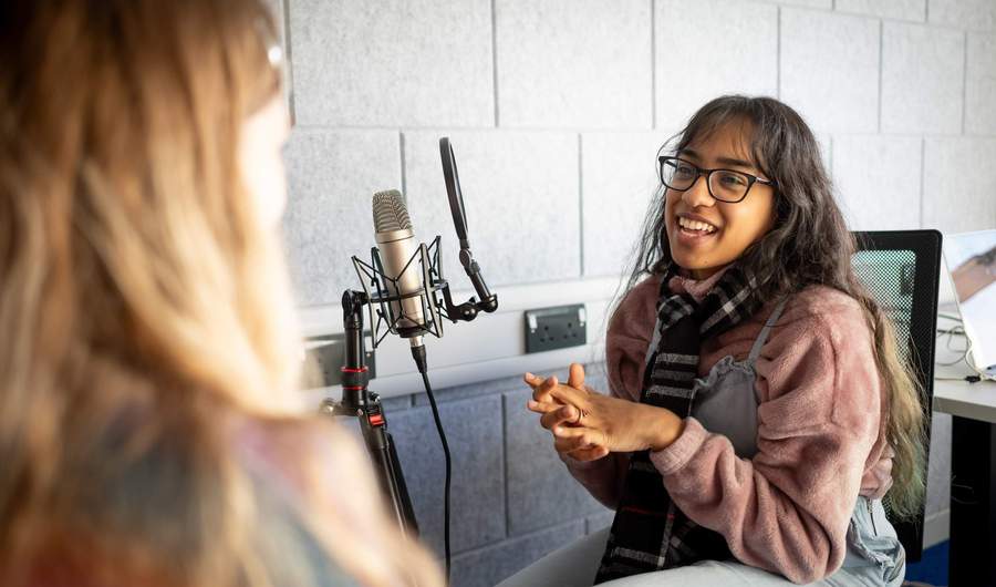 A person sits in front of a microphone while talking to another person.