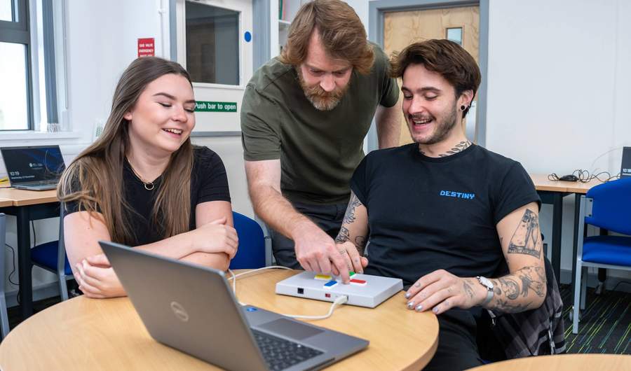 A person sits at a round table. In front of them is a small box with four buttons on it, connected to a laptop computer.