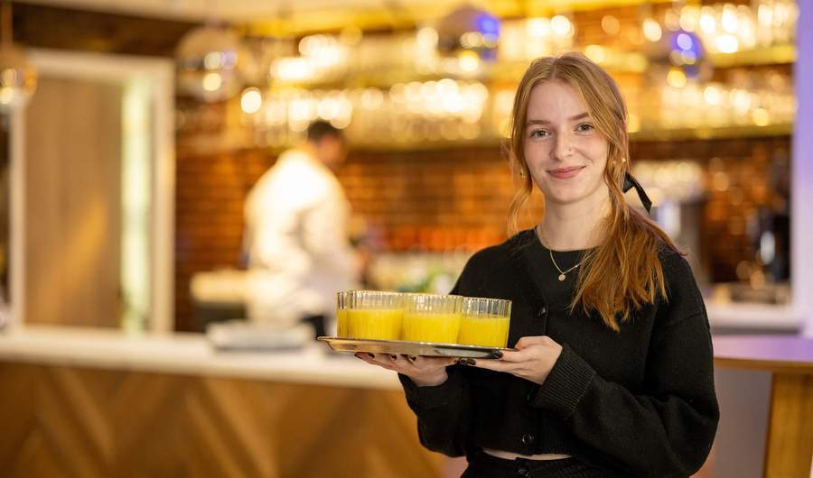 A person holding a tray of drinks. Behind them is a bar area.