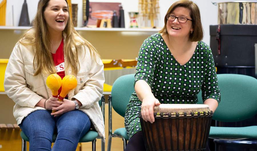 Two people sit in chairs, each holding a percussion musical instrument.
