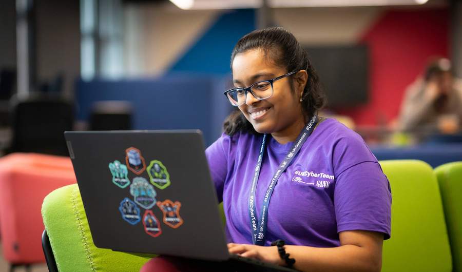 A person sits on a couch with a laptop computer resting on their knee.