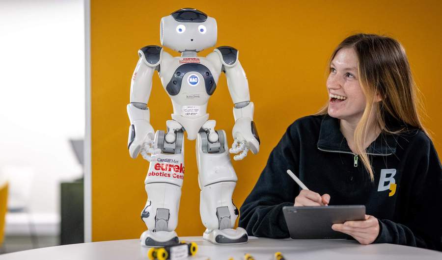 Person holding a tablet and stylus while looking up at a small humanoid robot.