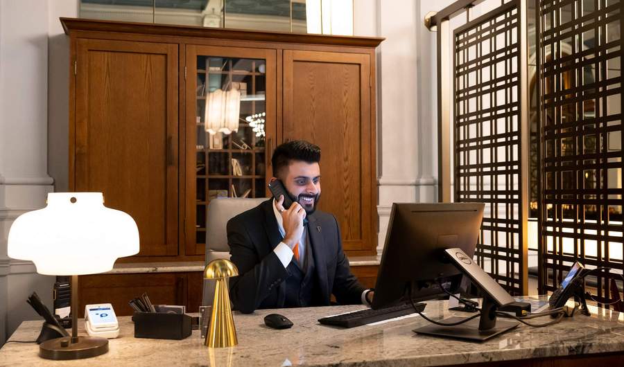 A person sits at a desk in a stylish hotel, talking on the phone.