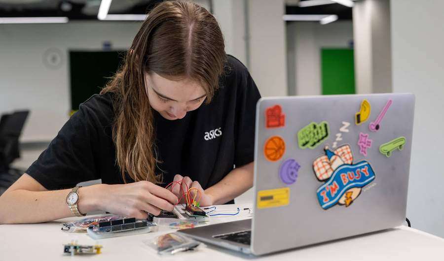 A person assembles electronics in front of a laptop computer.