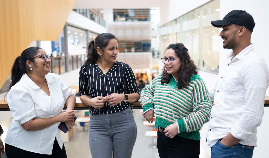 Four people talking to each other on a balcony in an atrium space.