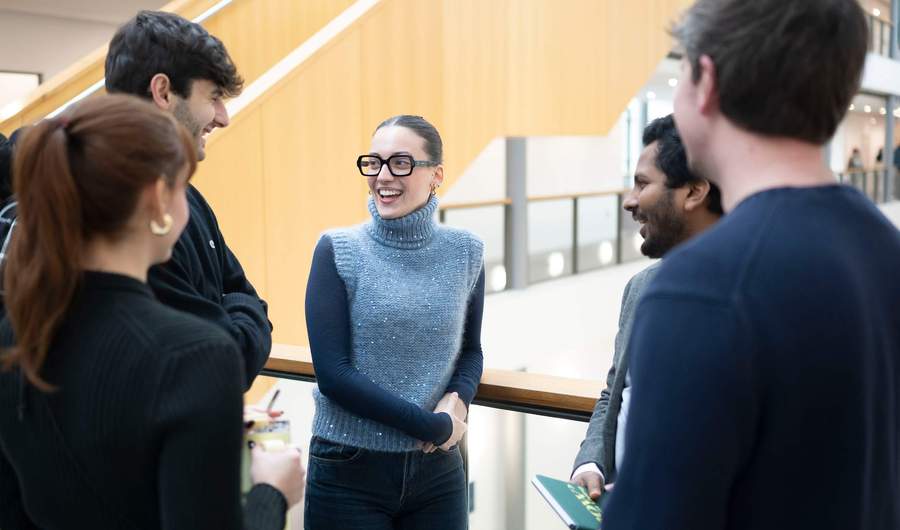 Five people talking to each other on a balcony in an atrium space.