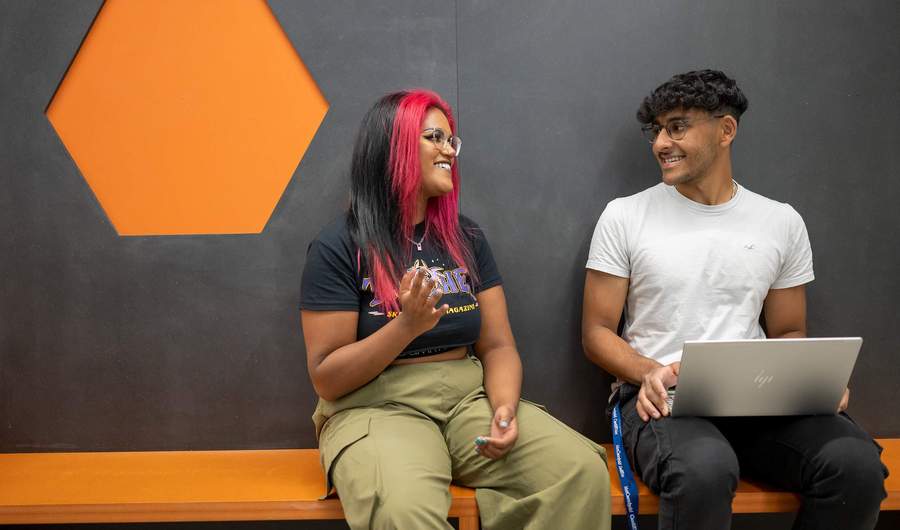 Two people talking while sat next to each other on a colourful bench.