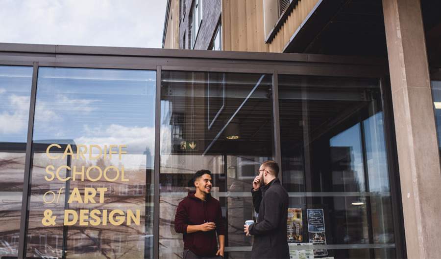 Two students talk outside the glass entrance to the Cardiff School of Art and Design