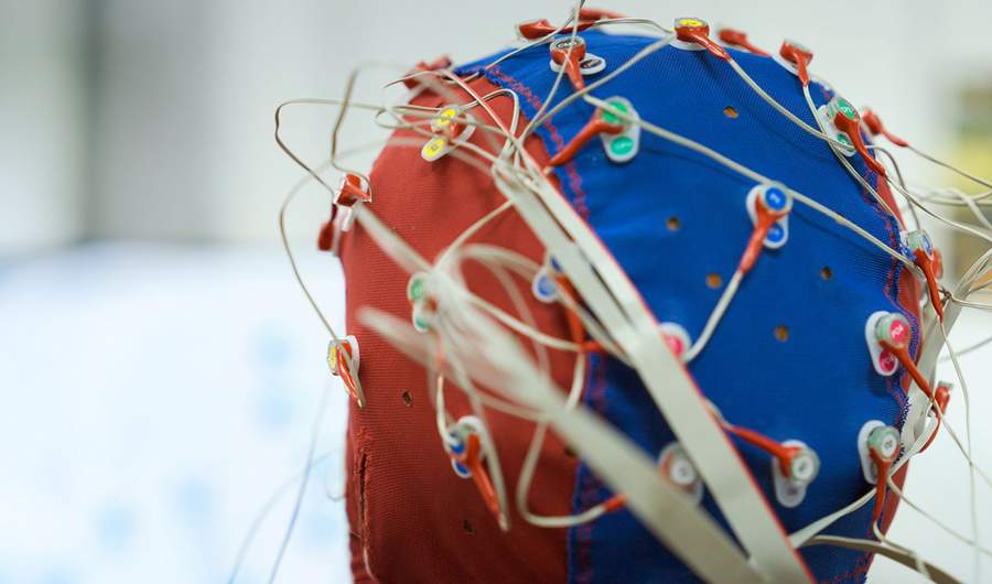 A close-up of a person wearing a skull cap fitted with electrical sensors connected to wires.