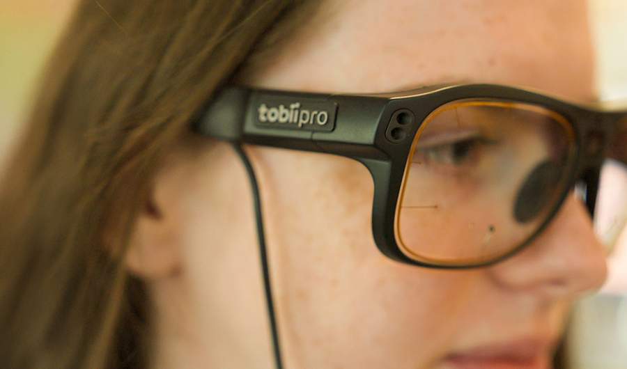 A close-up of a person wearing glasses. The glasses appear to have sensors on the front and a wire attached to the frame.