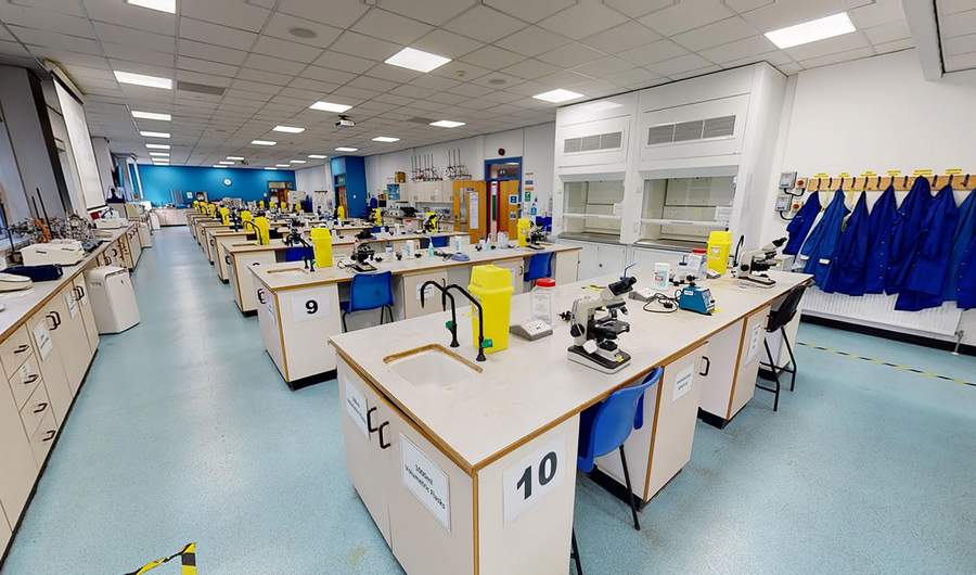 Rows of workbenches in a large laboratory. On the workbenches are microscopes and other scientific equipment.