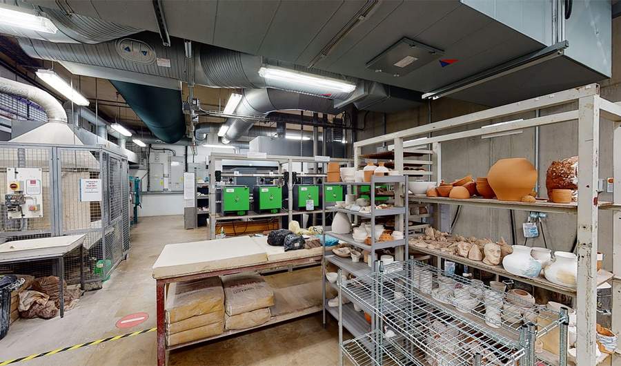 Shelves of completed ceramics in front of work tables and supply shelves