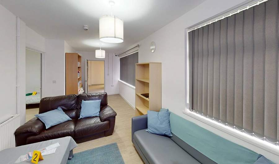 A living room with two sofas and low table. On the table, alongside some pieces of paper, is a small sign with the number two on it.