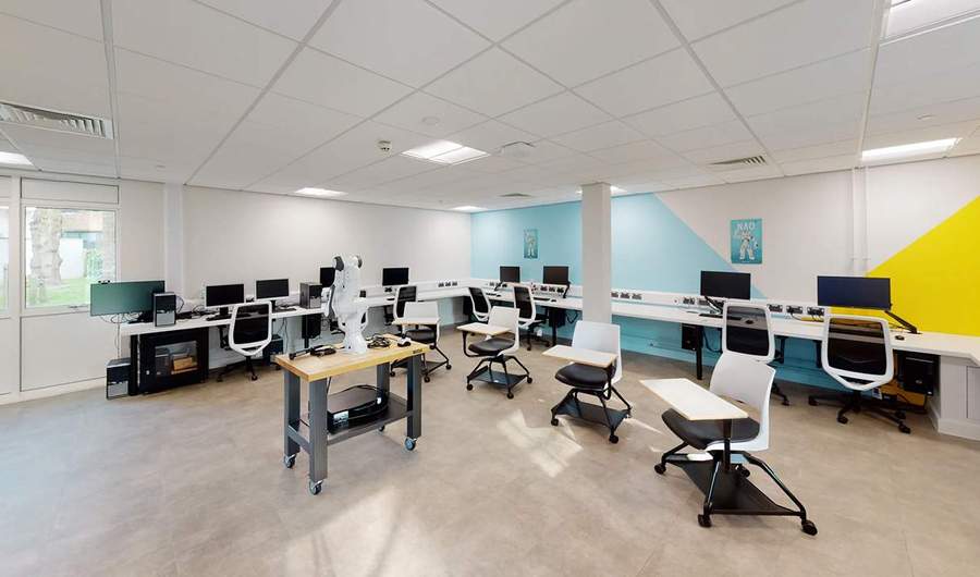 A bright open space with computer desking running along the walls. In the centre of the room is a table with a robotic arm.