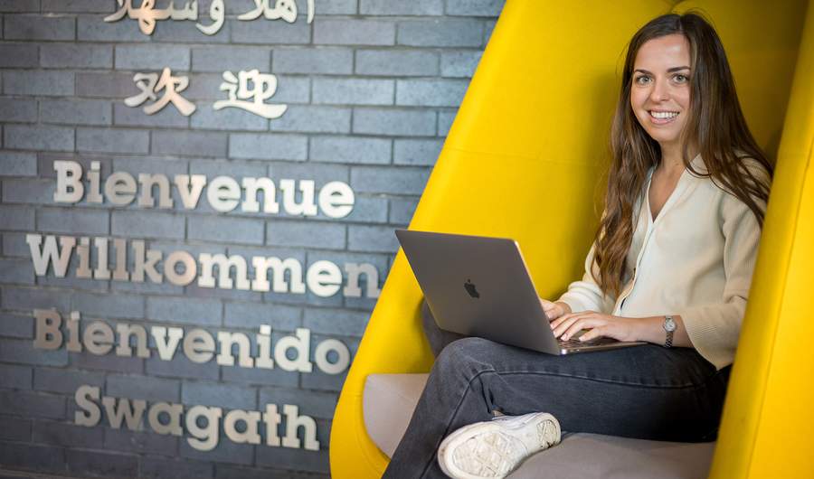 A woman working on her laptop while comfortably seated in a bright yellow chair, showcasing a lively atmosphere.