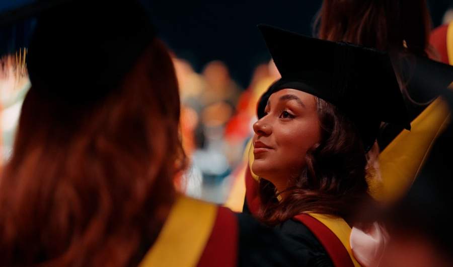 A woman in a graduation gown and cap smiles at the camera, celebrating her academic achievement.