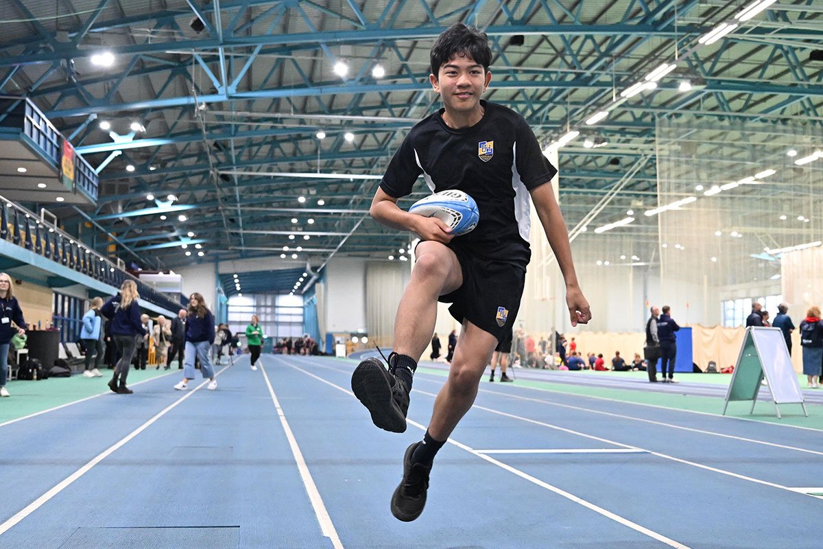 School pupil running with rugby ball on the running track inside the National Indoor Athletics Centre at Cardiff Metropolitan University's Cyncoed campus