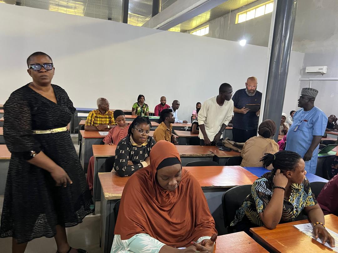 A large group of adult learners sit at desks in a classroom